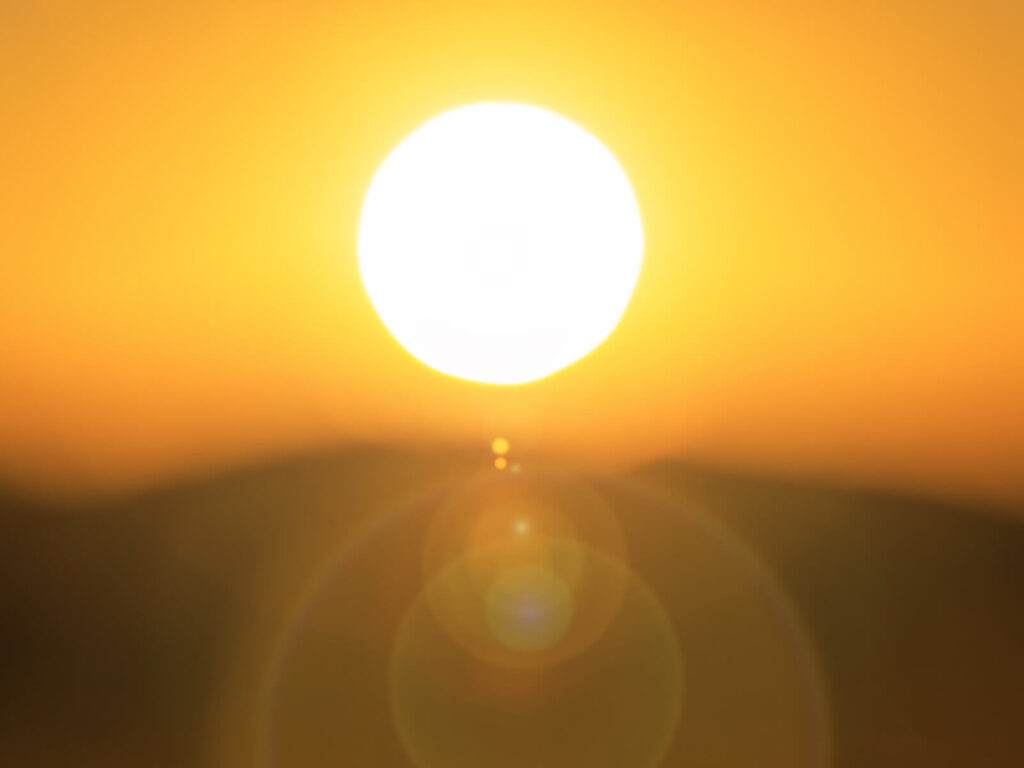 Strahlende Sonne mit warmem Lichtschein am Himmel, Symbol für Sonnenschutz und angenehmes Terrassenklima